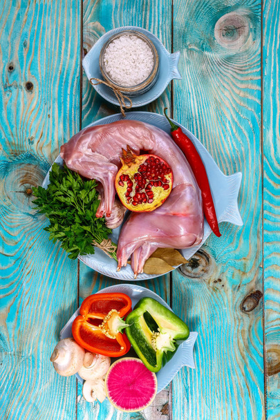 野菜やキノコと生のウサギの肉は、木製の青の背景に円に描かれています。料理の背景。上部表示、垂直画像. - 写真・画像