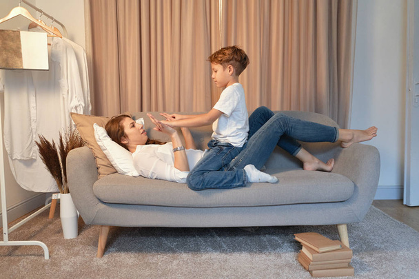Wstępnie teen chłopiec bawi się z jego matką w domu na kanapie - Zdjęcie, obraz