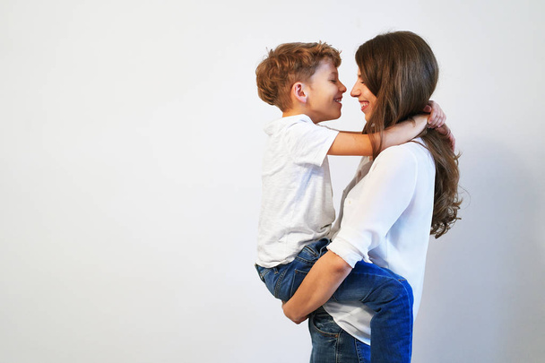 Молодая мать, держа своего маленького сына улыбается и глядя ему в глаза на белом фоне с копией пространства
 - Фото, изображение