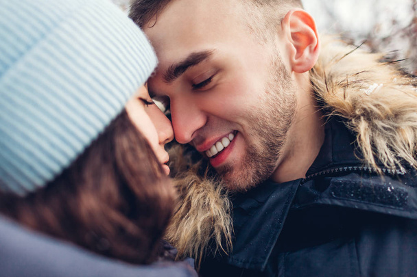 Прекрасная любящая пара обнимается в зимнем лесу. Люди трогают носы и улыбаются. Закрыть
 - Фото, изображение