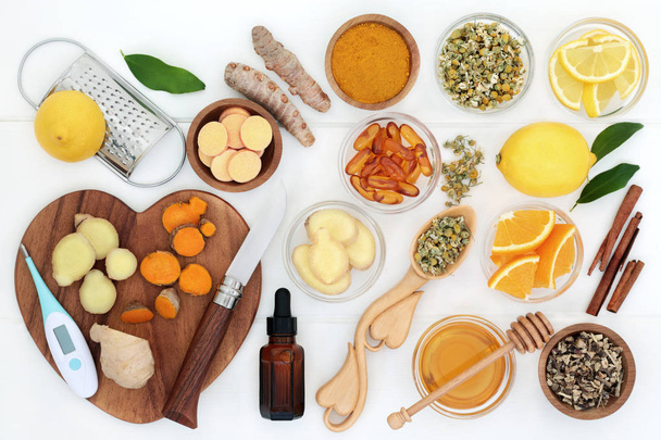 Ingredients for cold and flu remedy with thermometer, ginger, turmeric, echinacea, chamomile, cinnamon, eucalyptus oil, honey, vitamin tablets and capsules with orange and lemon fruit on white wood. - Photo, Image