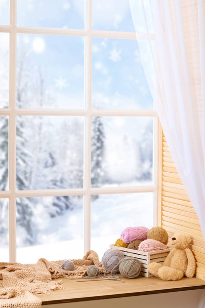 Шерстяная пряжа и ткань на подоконнике. Красивый вид за окном - зимний пейзаж и снег
. - Фото, изображение