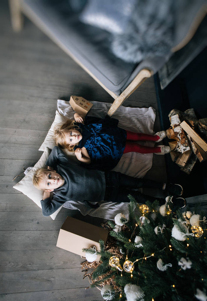 children - a boy and a girl are lying by the fireplace, Christmas tree and cardboard houses, cozy Christmas decor and children's emotions - Foto, immagini