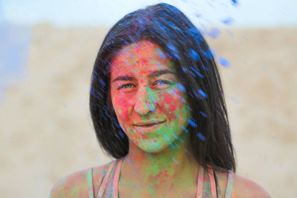 Closeup portrait of gorgeous brunette woman covered with colorful Holi paint, posing at the desert - Photo, Image