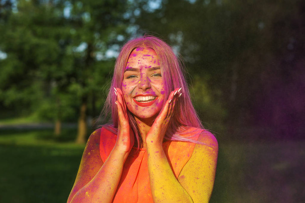 Attractive blonde girl having fun with colorful dry paint at the park. Concept for festival Holi - Photo, Image