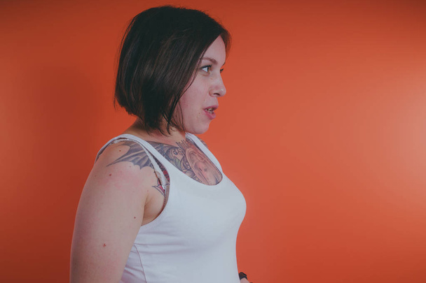 Girl with a tattoo on her chest, posing on an orange background - Photo, image