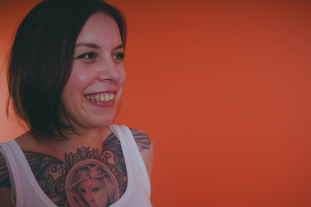 Girl with a tattoo on her chest, posing on an orange background - Zdjęcie, obraz