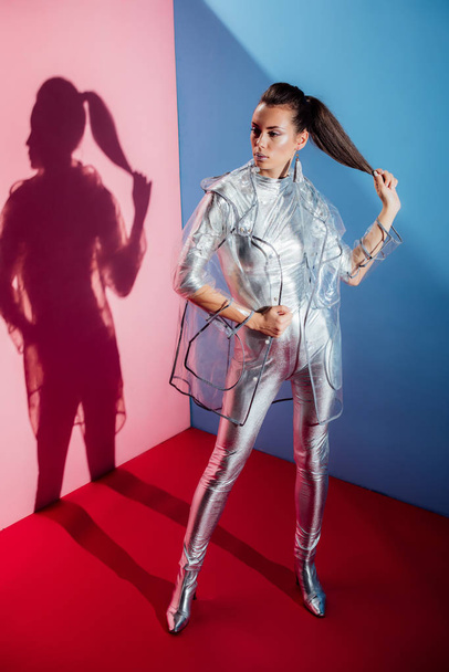 стильная девушка позирует в металлическом боди и модном плаще для модной съемки на розовом и синем фоне
 - Фото, изображение
