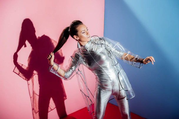 beautiful elegant girl posing in metallic bodysuit and trendy raincoat for fashion shoot on pink and blue background - Fotoğraf, Görsel