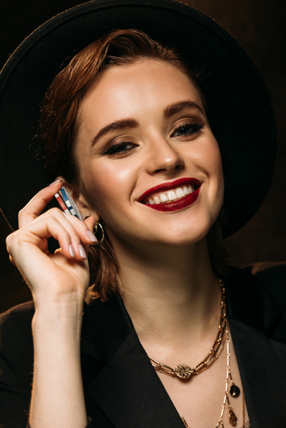 happy attractive girl in jacket and hat holding poker chips and looking at camera - Foto, imagen