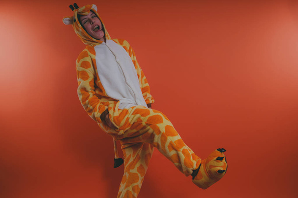pajamas in the form of a giraffe. emotional portrait of a girls on an orange background. crazy and funny girl in a suit. animator for children's parties - Fotó, kép