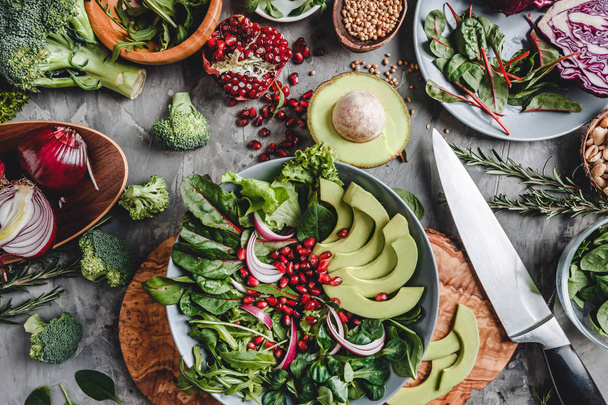 Gesunder frischer Salat mit Avocado, Gemüse, Rucola, Spinat, Granatapfel im Teller vor grauem Hintergrund. Gesunde vegane Ernährung, saubere Ernährung, Diät, Draufsicht - Foto, Bild