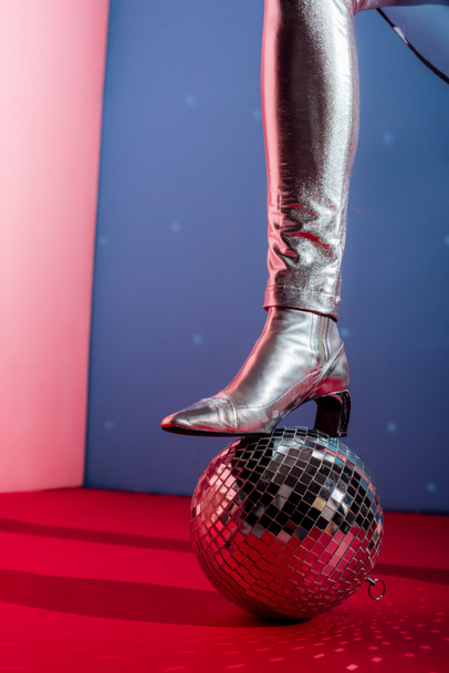 partial view of woman in metallic footwear posing with disco ball on pink and blue background - Photo, Image
