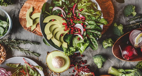 健康的なサラダとアボカド、緑、ルッコラ、ほうれん草、灰色の背景の上のプレートにザクロ。健康ビーガン フード、きれいな食事、ダイエット、平面図、調子を整える - 写真・画像