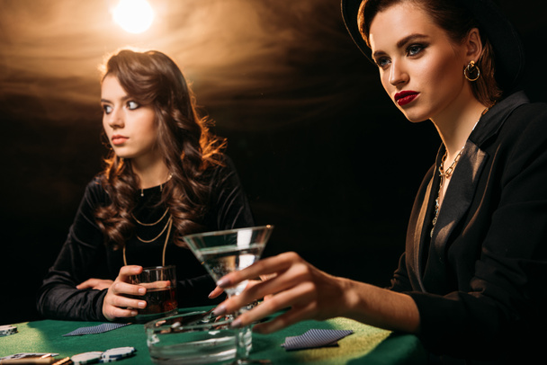 カジノ、カクテルのガラスを保持している女性でのテーブルでポーカーをプレイする魅力的な女の子 - 写真・画像