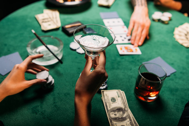 περικομμένη εικόνα μιας γυναίκας κι ενός άνδρα παίζει τραπέζι πόκερ στο καζίνο, κρατώντας το ποτήρι αλκοόλ κοκτέιλ κορίτσι - Φωτογραφία, εικόνα