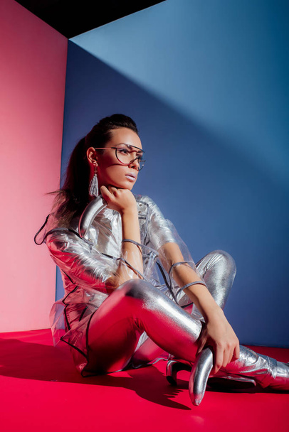 fashionable elegant woman in metallic bodysuit posing with silver bananas on pink and blue background - Foto, Imagem