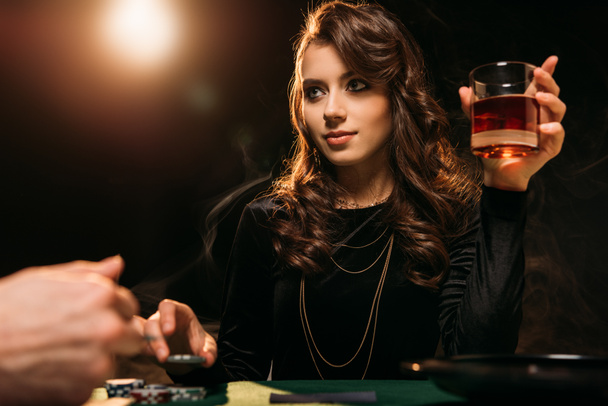 low angle view of attractive girl holding glass of whiskey at poker table in casino - Photo, Image