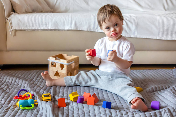 Симпатичный маленький мальчик с синдромом Дауна играет в игрушки дома
 - Фото, изображение