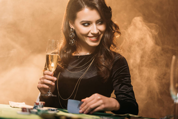 aantrekkelijk meisje bedrijf glas champagne aan de pokertafel in casino glimlachen en op zoek weg - Foto, afbeelding
