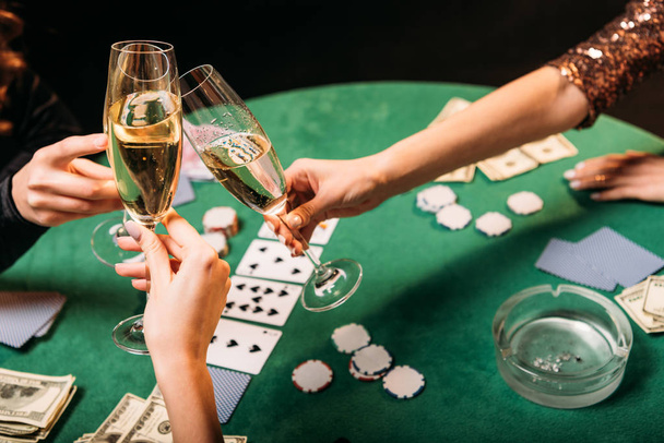 cropped image of girls clinking with glasses of champagne at poker table in casino - 写真・画像