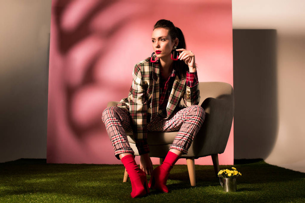 attractive elegant girl in checkered suit posing in armchair on pink background - Valokuva, kuva