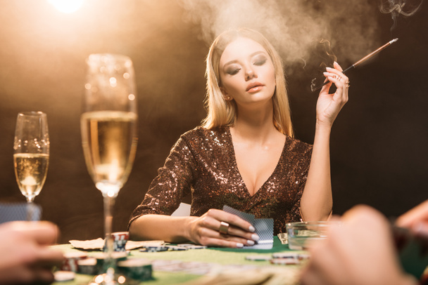 selective focus of attractive girl smoking cigarette at poker table in casino - Photo, Image