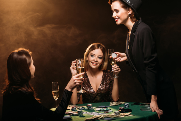 happy beautiful women with glasses of champagne talking at poker table in casino - Photo, Image