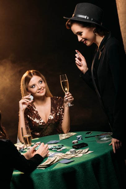 glimlachend aantrekkelijke meisjes met glazen champagne praten op de pokertafel in casino - Foto, afbeelding