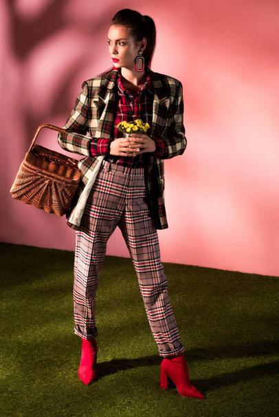 belle fille élégante en costume à carreaux automne posant avec panier et fleurs sur rose
 - Photo, image