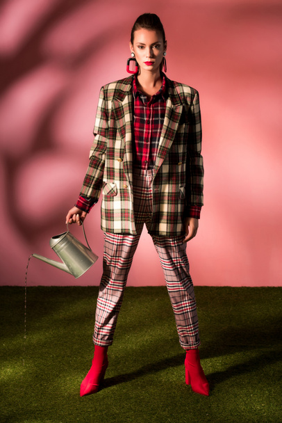 beautiful stylish girl in autumn checkered suit posing with watering can on pink - Foto, Bild