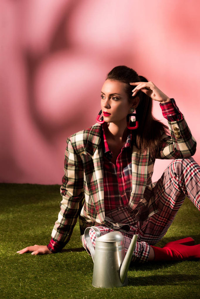 stylish woman in autumn checkered suit sitting on green carpet with watering can - Фото, изображение