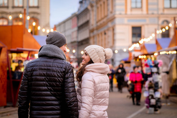 Una giovane coppia romantica indossa abiti invernali passeggiando in strada serale con la fiera di Natale
 - Foto, immagini