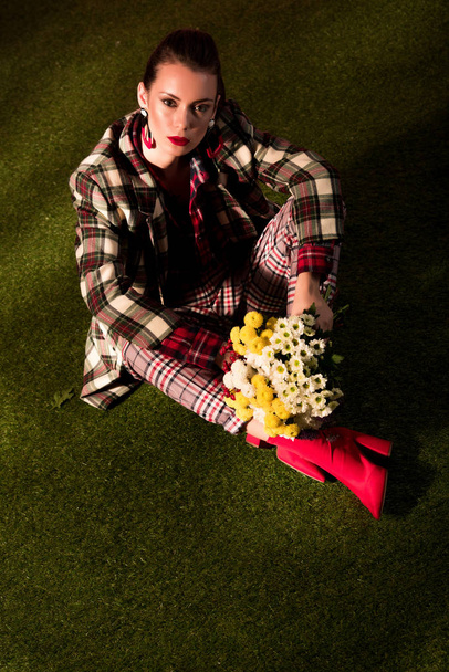 élégante jeune femme élégante en costume à carreaux d'automne posant avec des fleurs sur tapis vert
 - Photo, image