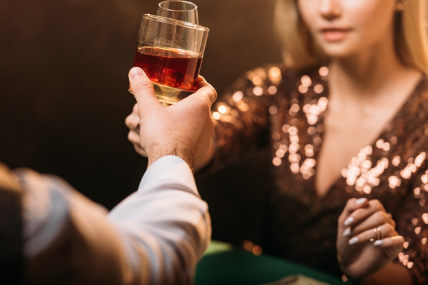 oříznutý obraz dívky a krupiér cinkání sklenic alkoholu pije při hraní pokeru v kasinu - Fotografie, Obrázek