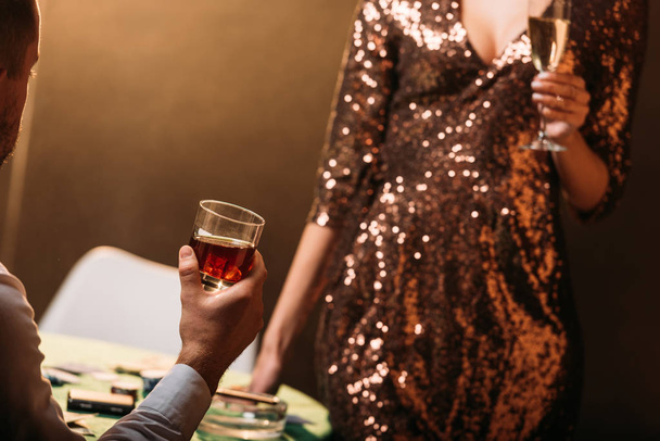 imagem cortada de menina e croupier segurando copos de bebidas alcoólicas na mesa de poker no cassino
 - Foto, Imagem