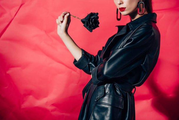 cropped view of model in black leather suit posing with black rose on red background - Fotografie, Obrázek