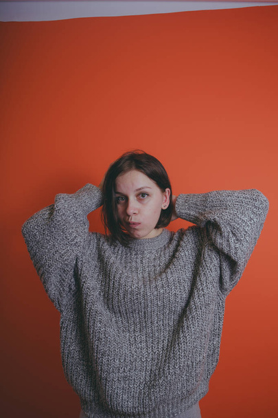 Young girl in warm grey sweater posing on orange background, woman with short haircut in knitted sweater, space for text - Foto, afbeelding