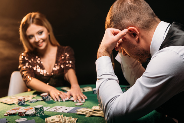 улыбающаяся привлекательная девушка берет фишки для покера и смотрит на грустного крупье в казино
 - Фото, изображение