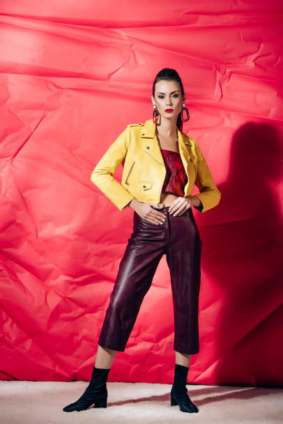 stylish brunette model posing in yellow leather jacket on red background - Foto, imagen