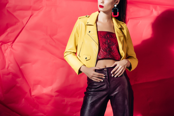 cropped view of stylish woman posing in yellow leather jacket on red background - Fotoğraf, Görsel