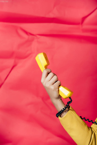 cropped view of woman holding yellow retro phone tube on red background - Fotoğraf, Görsel