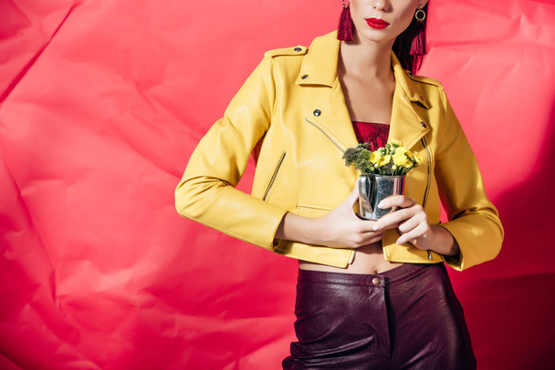 cropped view of woman in yellow leather jacket posing with flowers on red background - Foto, Bild