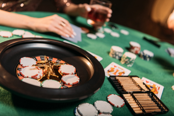 cropped image of girl playing poker at table in casino, roulette and cigars on foreground - Photo, Image