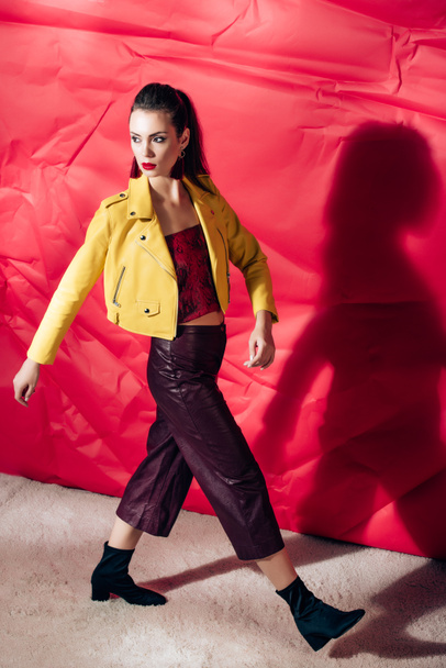 divatos lány pózol sárga bőr kabát divat lő a piros háttéren - Fotó, kép