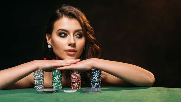 красива коричнева волохата дівчина спирається на покерні чіпи і дивиться ізольовано на чорному
 - Фото, зображення