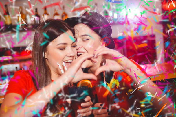 Confetti party. Two young lesbian girls make a heart with their hands at a club party. - Φωτογραφία, εικόνα