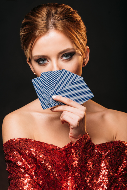 attractive girl in red shiny dress looking out from playing cards isolated on black - Фото, зображення