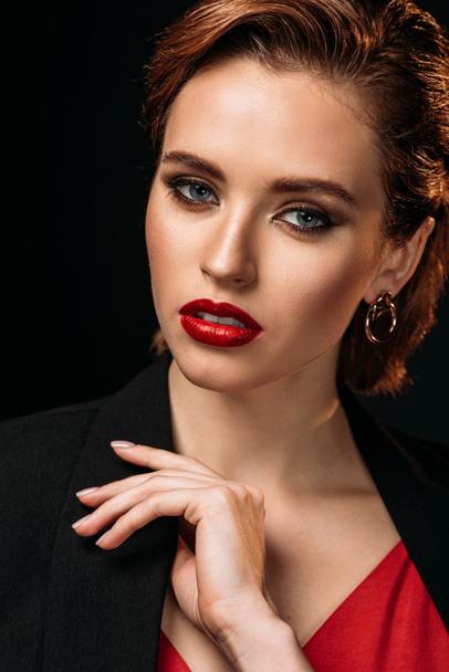 portrait of beautiful woman in red dress and black jacket looking at camera isolated on black - Фото, изображение