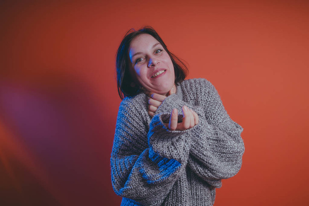 Young girl in warm grey sweater posing on orange background, woman with short haircut in knitted sweater, space for text - Foto, Bild